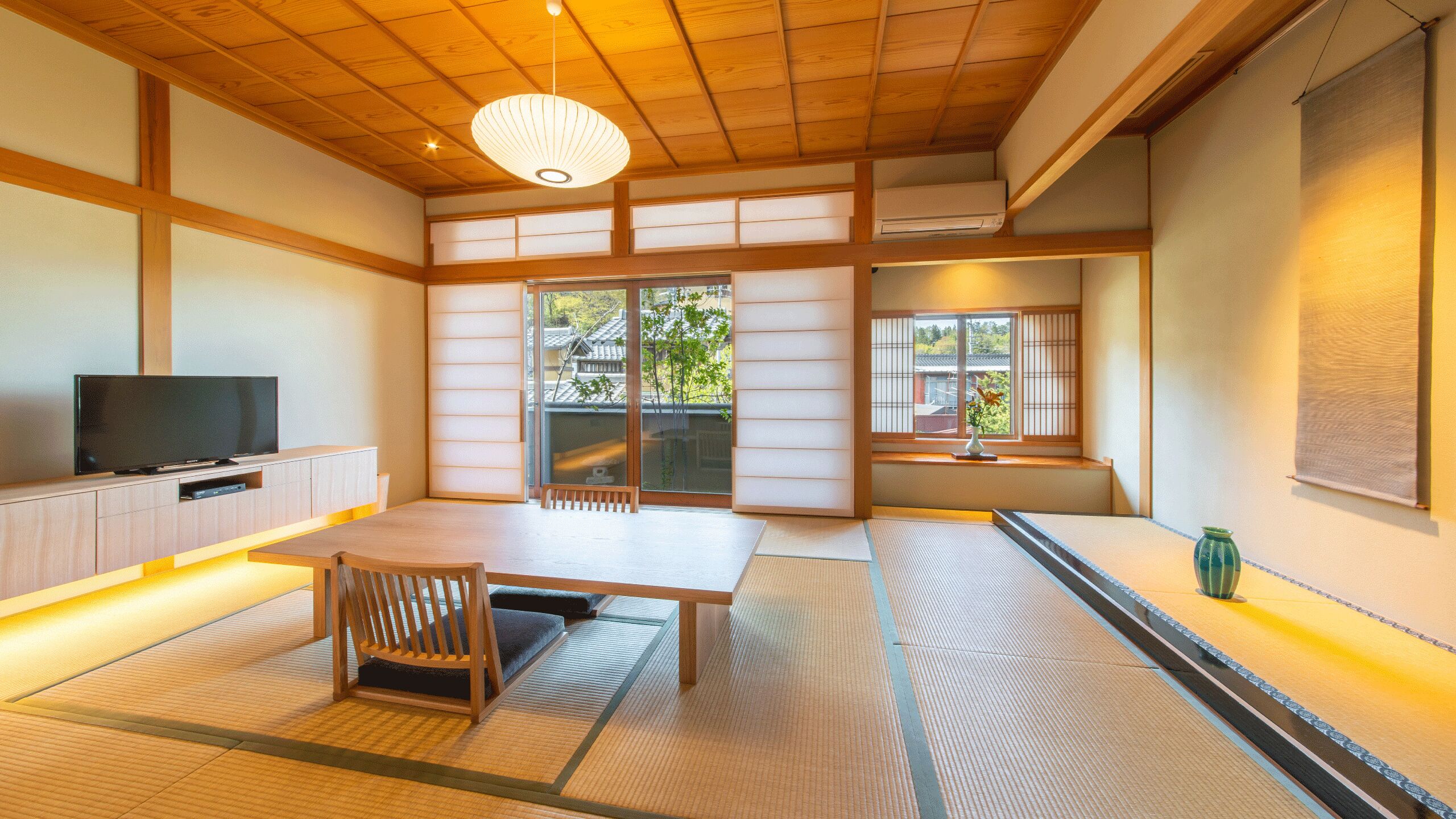 A traditional Japanese room with tatami flooring, a low table, a television, sliding doors, and a view of the outside.