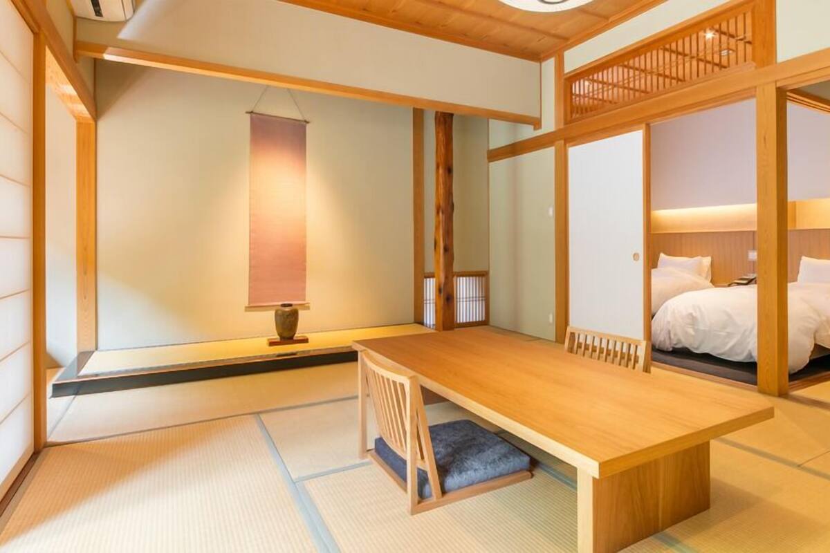 A traditional Japanese room with tatami flooring, a low wooden table, a bed with white bedding, and sliding doors.