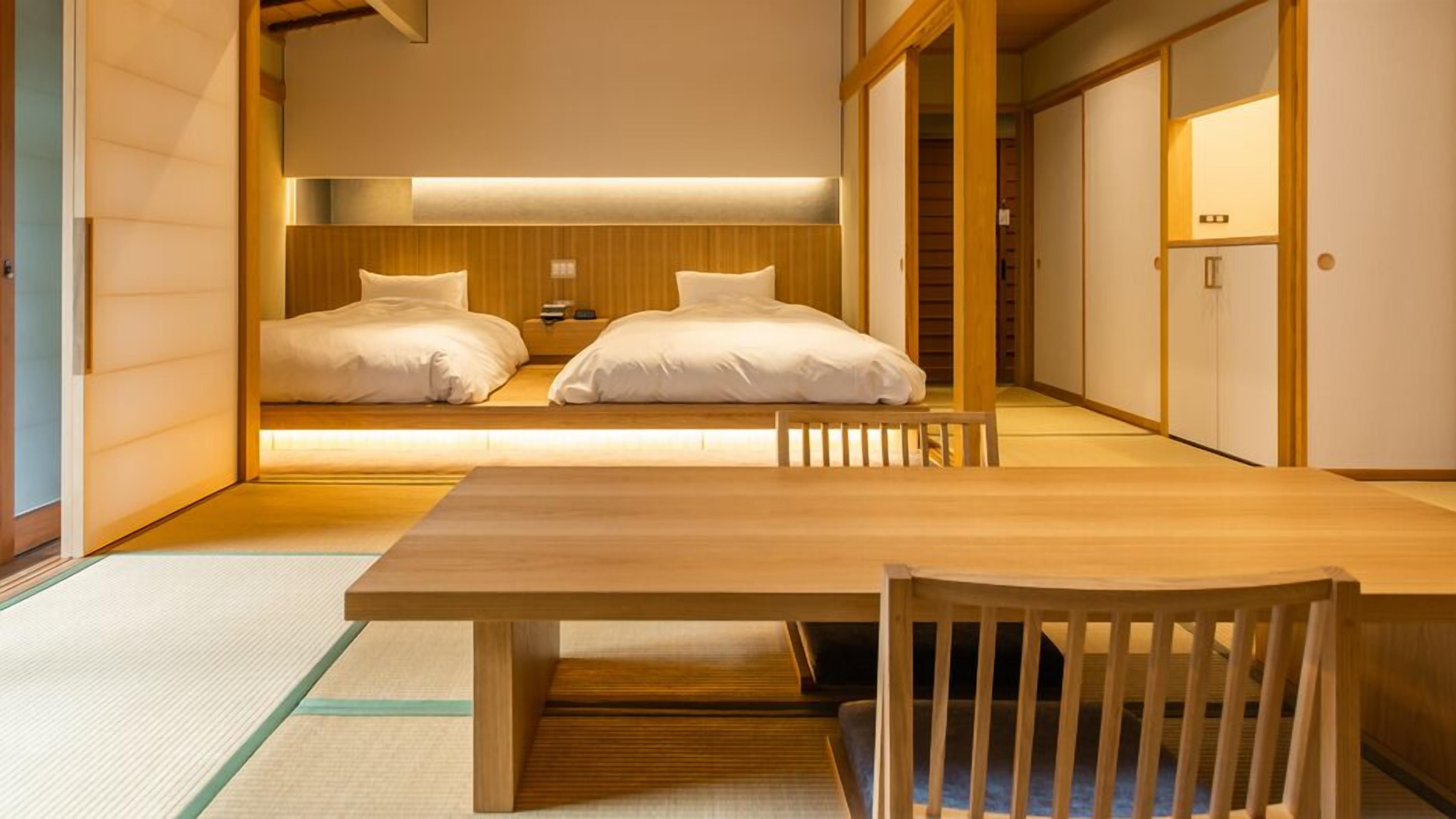 A traditional Japanese-style room with a wooden table and chairs, two beds with white bedding, and sliding doors.