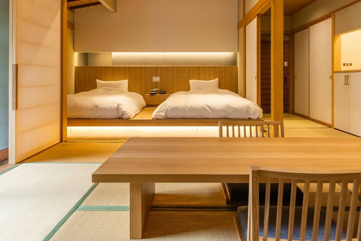 A traditional Japanese-style room with a wooden table and chairs, two beds with white bedding, and sliding doors.