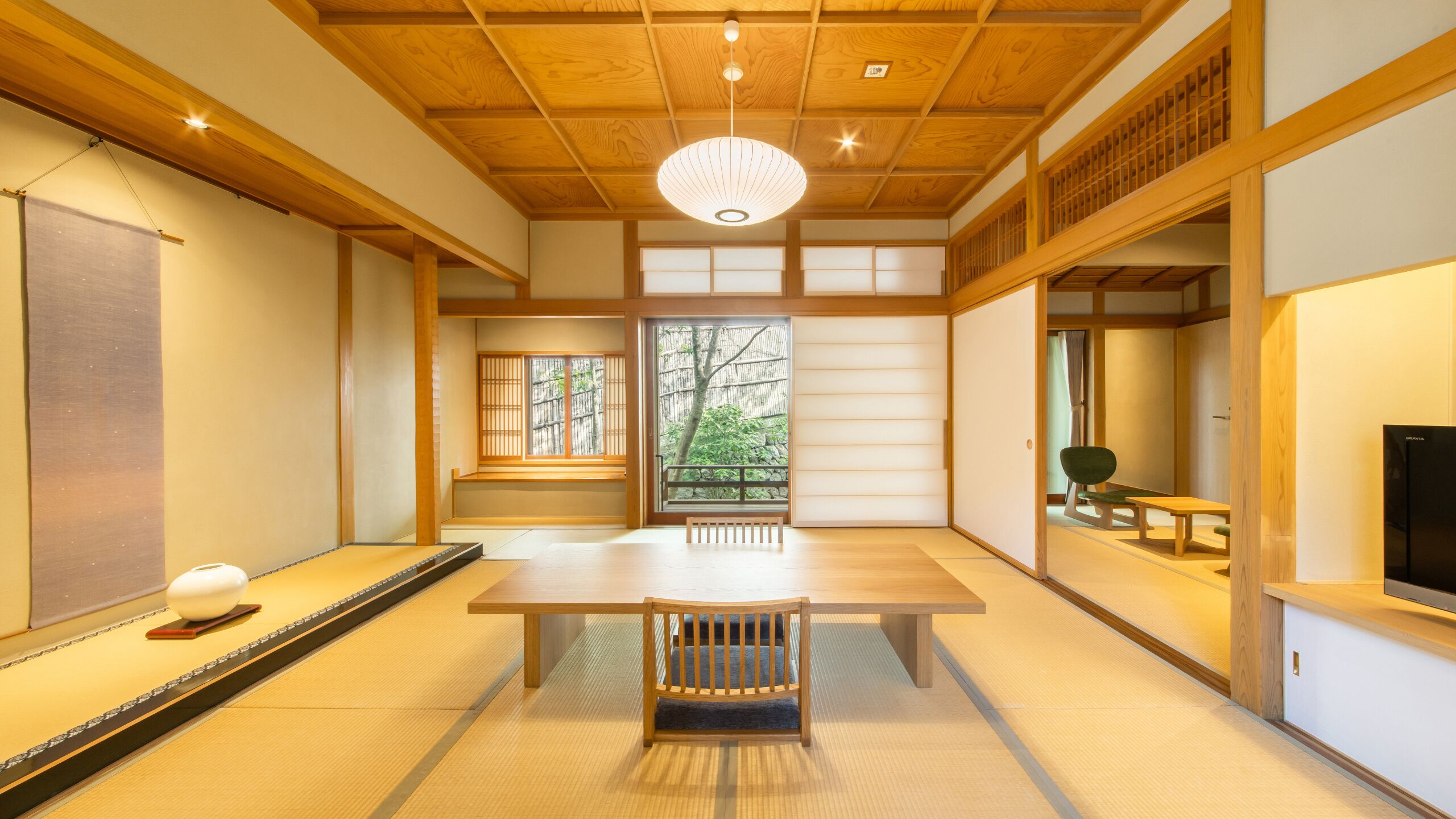 A traditional Japanese room with tatami flooring, a low wooden table, a bench, sliding doors, and a television.