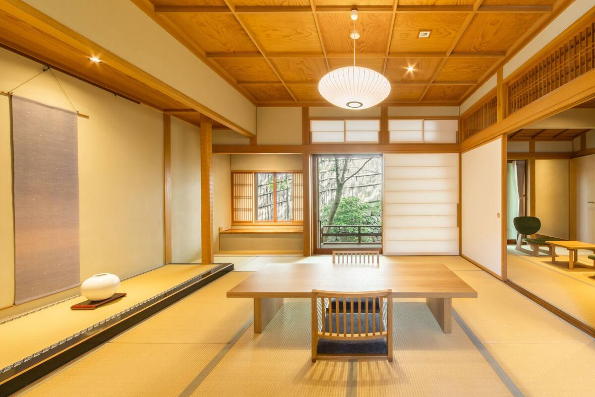 A traditional Japanese room with tatami flooring, a low wooden table, a bench, sliding doors, and a television.