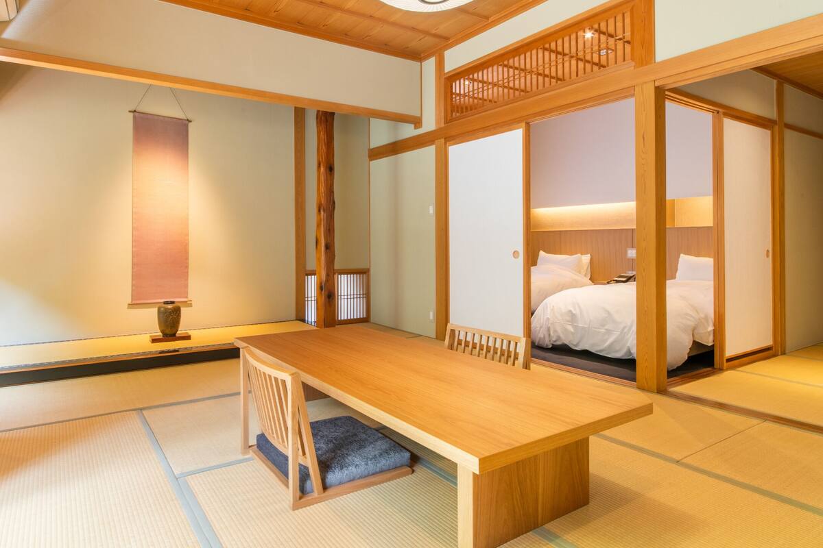 A traditional Japanese room with tatami flooring, a low wooden table, a bed with white bedding, and sliding doors.