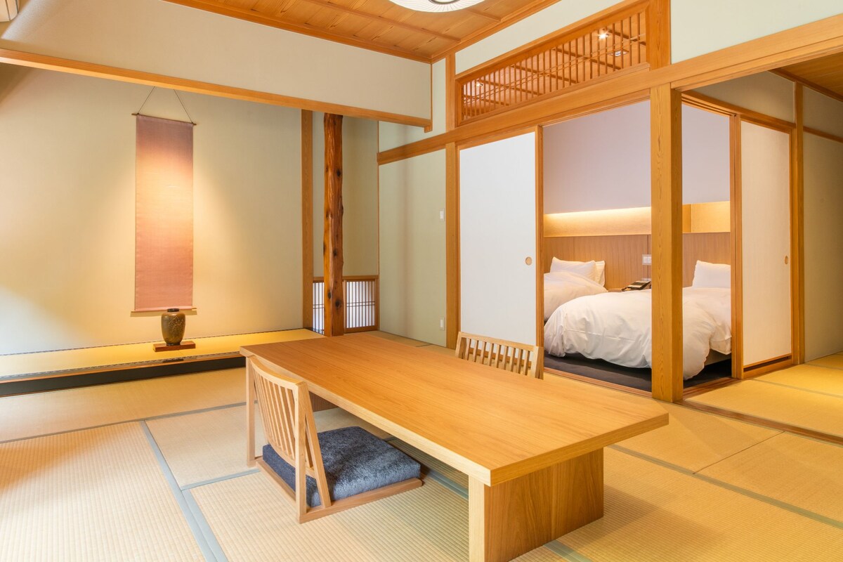 Ett traditionellt japanskt rum med tatamimattor på golvet, ett lågt träbord, en säng med vita sängkläder och skjutdörrar.