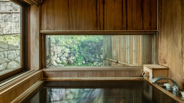 A wooden interior with a large window, a stone wall, and a wooden bench. - Kashiwaya Honten (Ueda)