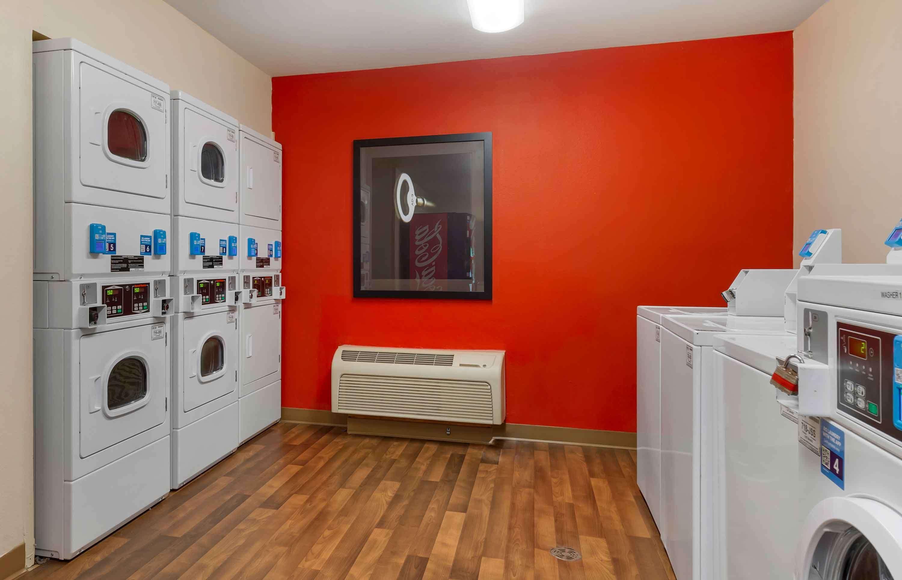 A laundry room with multiple washing machines and dryers, a red wall, and a framed picture.