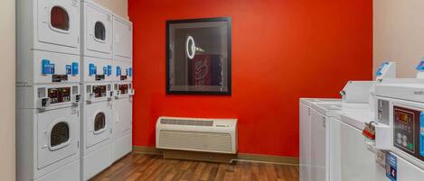 A laundry room with multiple washing machines and dryers, a red wall, and a framed picture.
