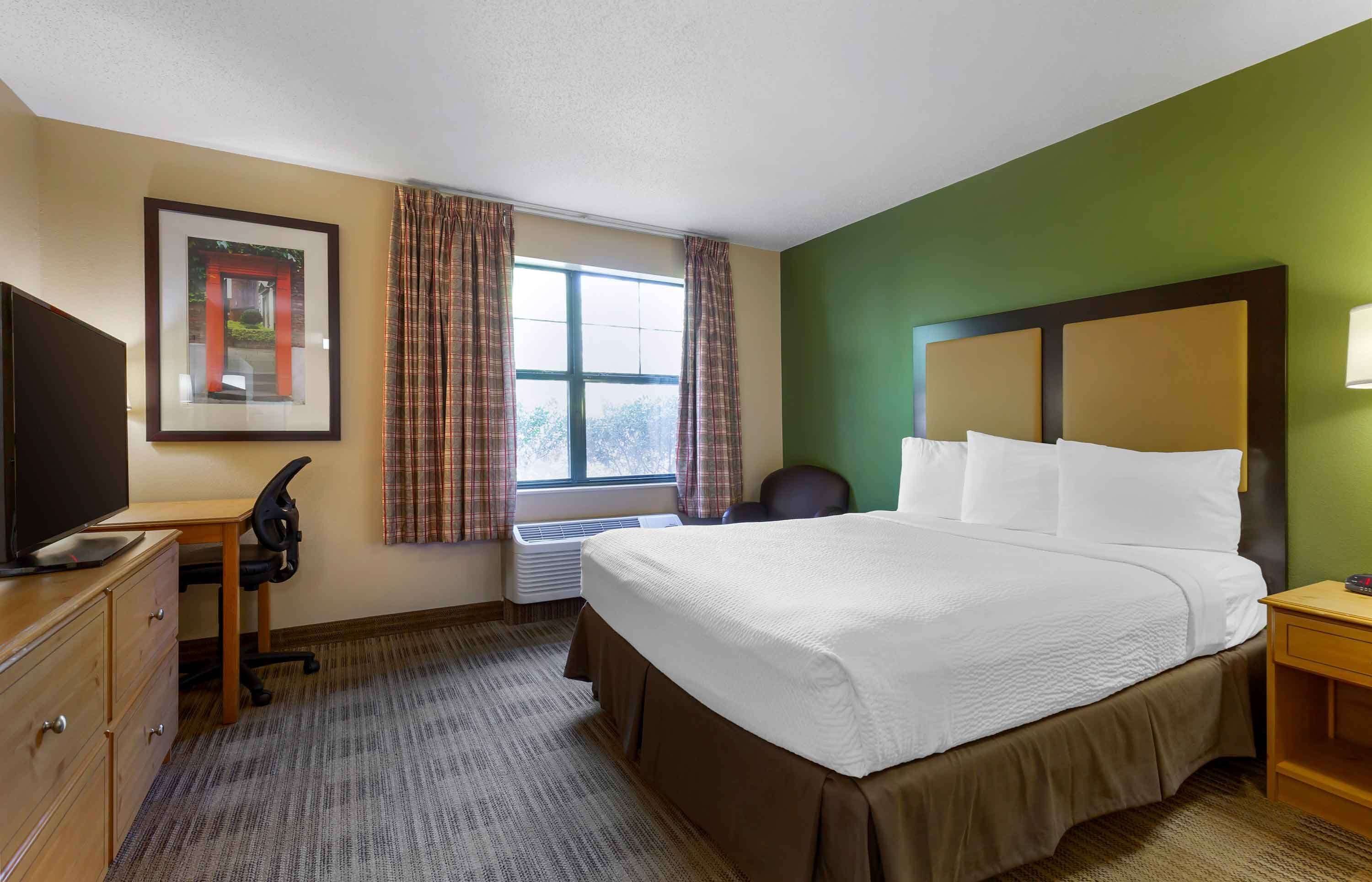 A hotel room with a bed, a desk, a chair, a television, and a window with curtains.