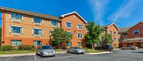 A multi-story building with a brick facade, parking lot, and several cars parked in front.