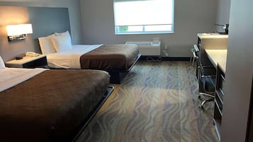 Habitación de hotel con dos camas, un escritorio, una silla, una ventana y una lámpara fijada a la pared.