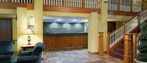 A hotel lobby with a reception desk, a staircase, and two armchairs.