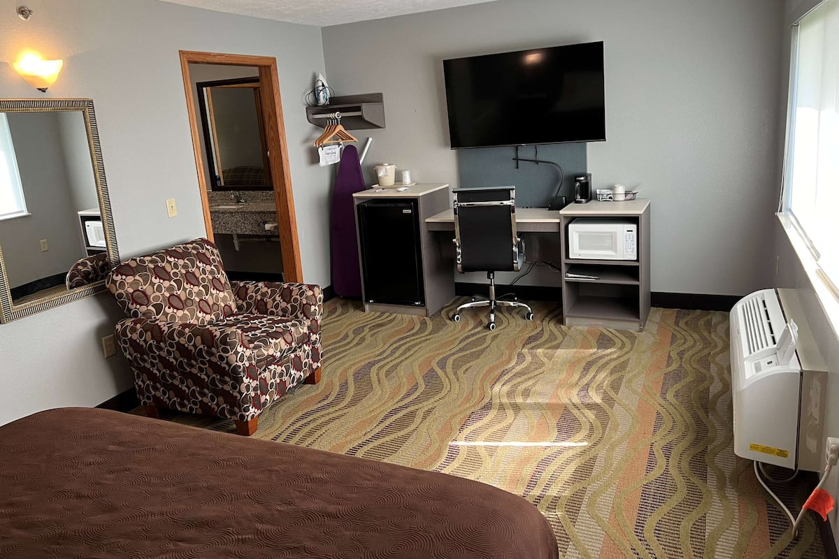 Ein Hotelzimmer mit einem Bett, einem Schreibtisch mit Computer, einem Fernseher, einer Mikrowelle und einem Heizgerät.