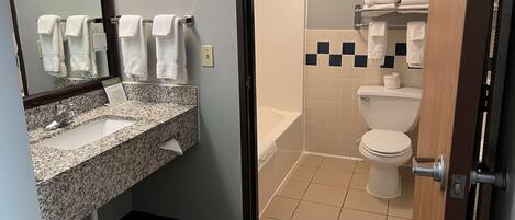 A bathroom with a granite sink, a mirror, a toilet, and a shower.