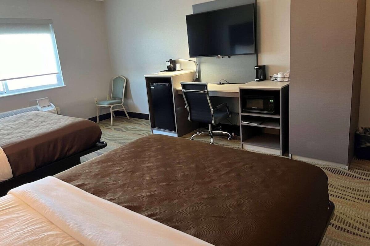 Ein Hotelzimmer mit zwei Betten, einem Schreibtisch mit Computer, einem Stuhl, einem Fernseher und einer Kaffeemaschine.