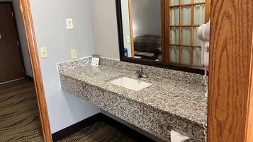 Baño con lavamanos de encimera de granito, espejo y dispensador de toallas.