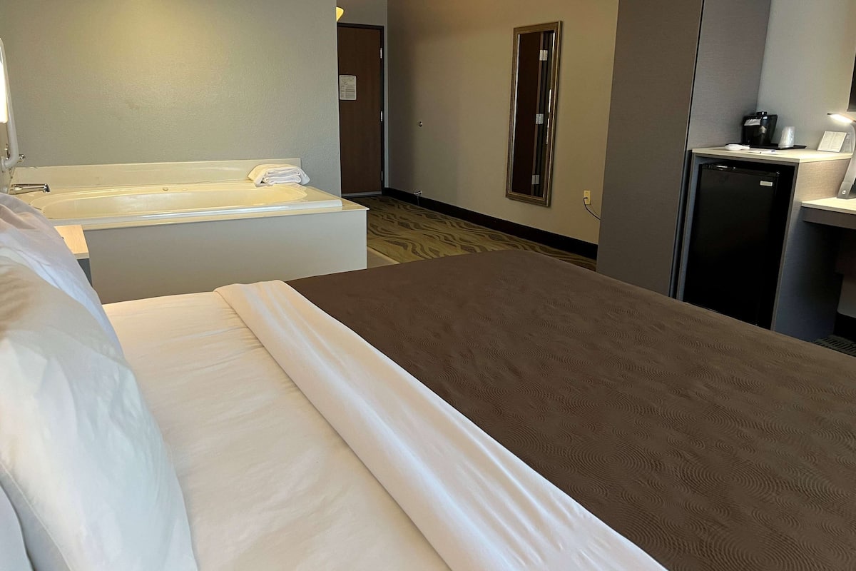 Ein Hotelzimmer mit Bett, Badewanne, Schreibtisch mit Kaffeemaschine und Kühlschrank.