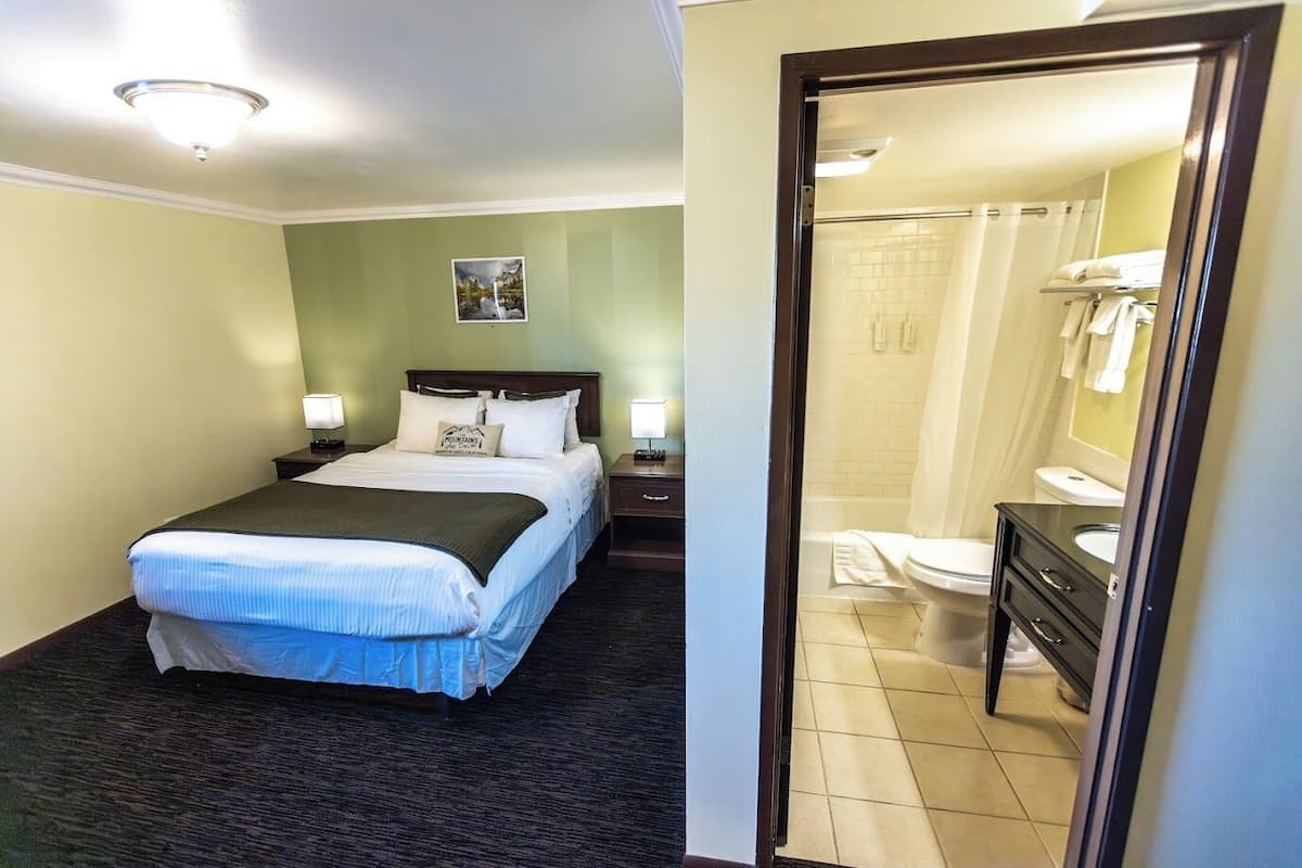 A hotel room with a bed, nightstands, a painting, a bathroom with a toilet, sink, and mirror.