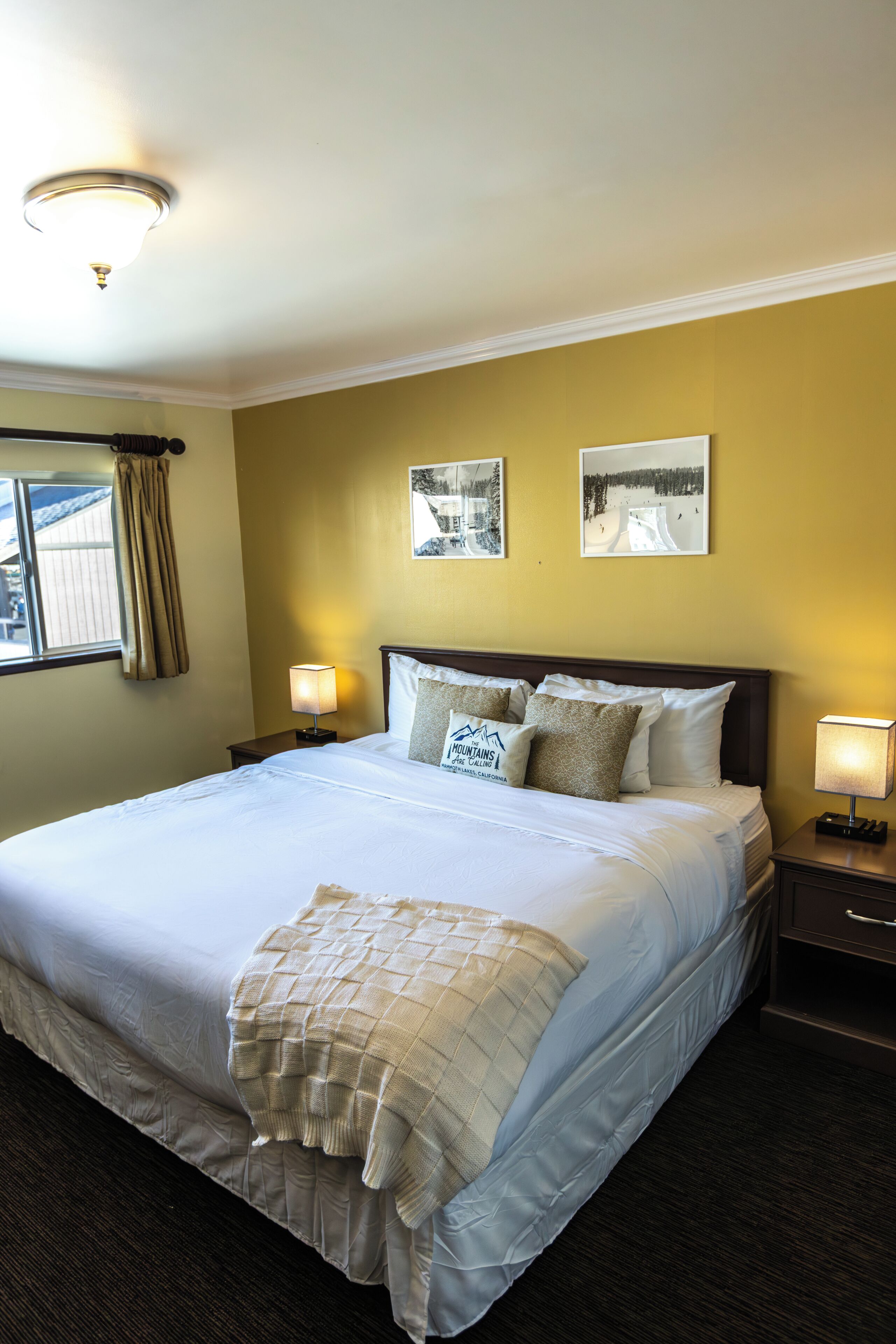 A hotel room with a large bed, two bedside lamps, a headboard with a logo, and two framed pictures on the wall.