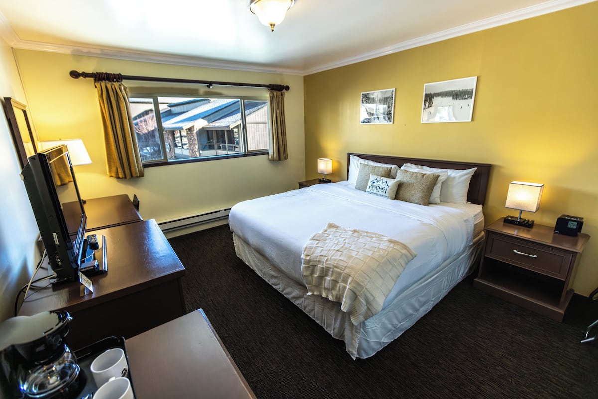 A hotel room with a bed, bedside tables, a desk with a computer, and a window with curtains.