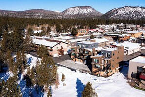 A snow-covered town with modern buildings, including a multi-story hotel with balconies and a parking lot. - The Mammoth Creek Inn (Mammoth Lakes)