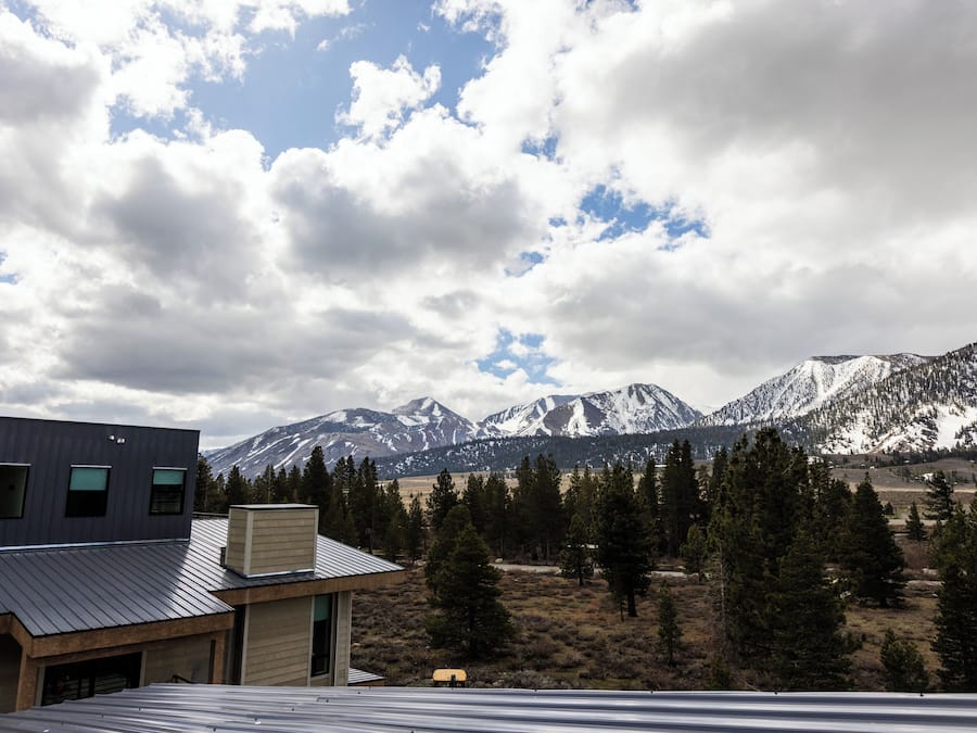 A modern building with a metal roof, surrounded by a forest and snow-capped mountains in the background.