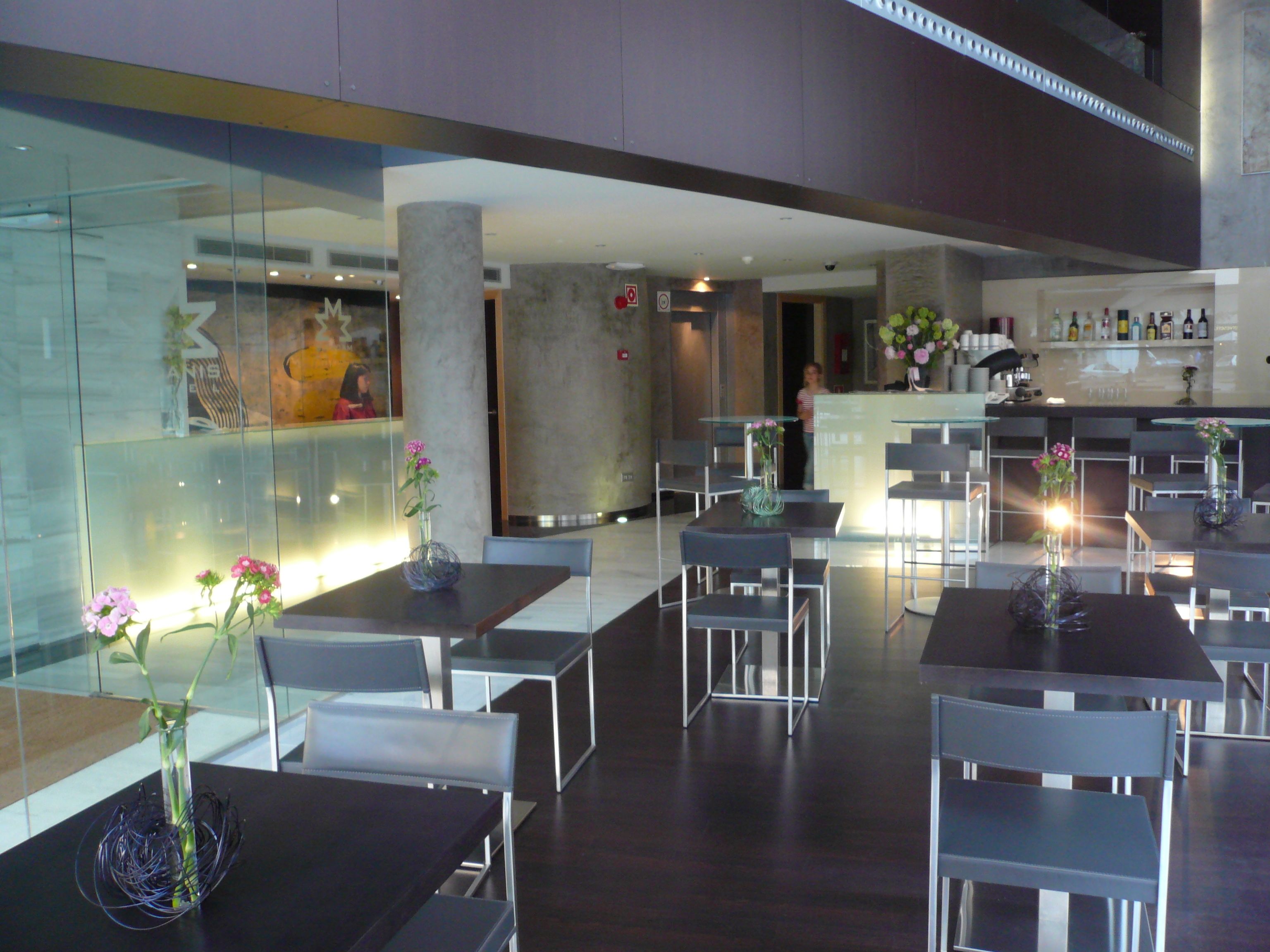 A modern restaurant with glass partitions, dark wooden tables, and chairs. There are vases with flowers on each table.