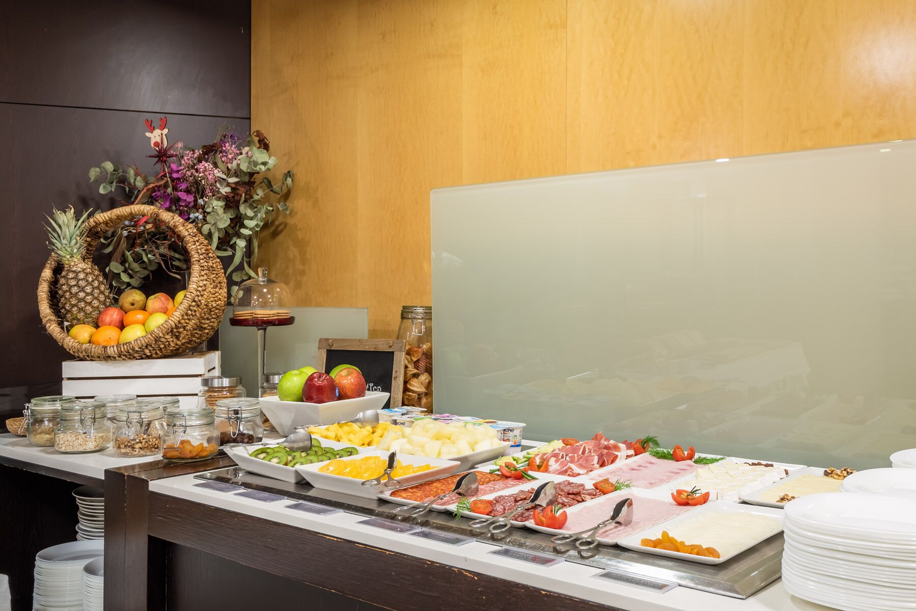 Un bufé con diversos alimentos, como frutas, quesos y carnes, dispuesto en un mostrador con un fondo de madera.