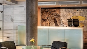 A reception area with a marble wall, a glass-top table with a vase of flowers, and two upholstered chairs. - Hotel Madanis (L'Hospitalet de Llobregat)