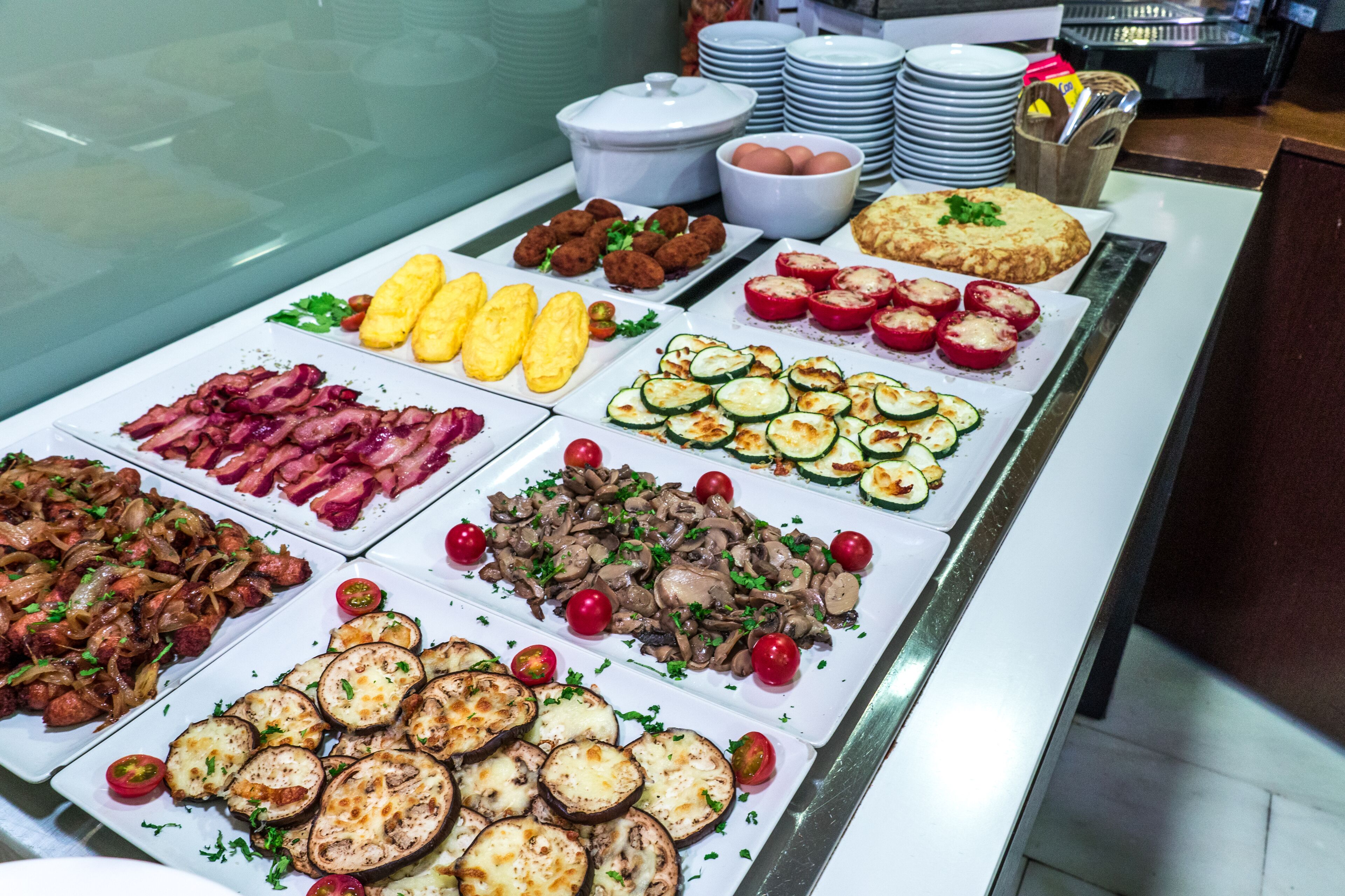 Een ontbijtbuffet met diverse gerechten, zoals spek, eieren en groenten.