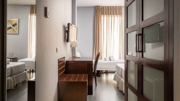 Een hotelkamer met een houten bankje, twee bedden, een bureau en een groot raam met gordijnen.
