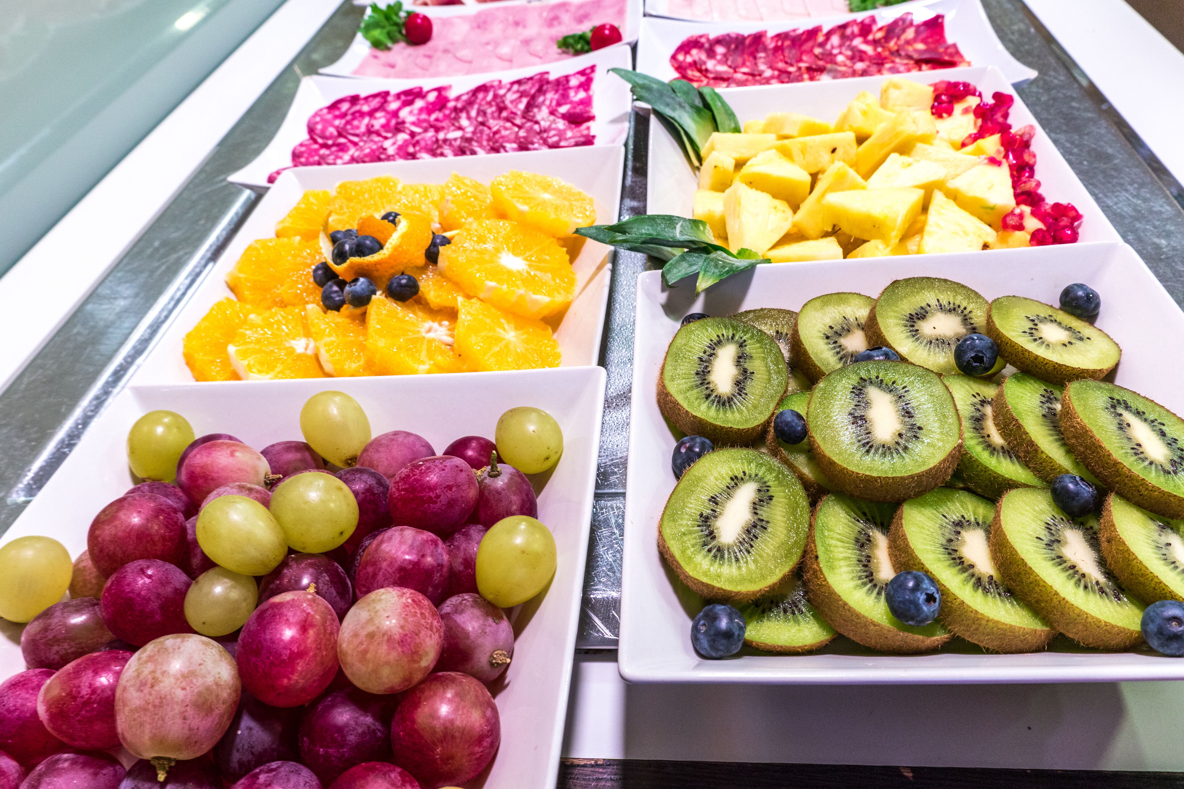 A buffet with various fruits including grapes, oranges, kiwi, and mangoes.