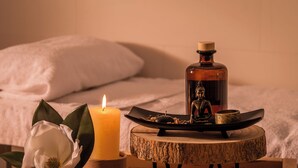 A candle, a Buddha statue, and a tray with nuts on a wooden table in a room with a bed and pillows. - Hotel Madanis (L'Hospitalet de Llobregat)