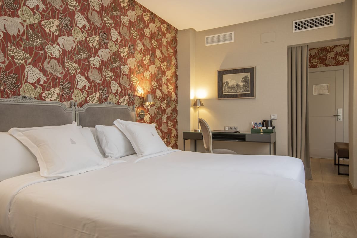 A hotel room with a large bed, a desk, a chair, and a door.