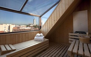 A wooden sauna room with benches and a large window offering a city view. - Hotel Meninas (Madrid)