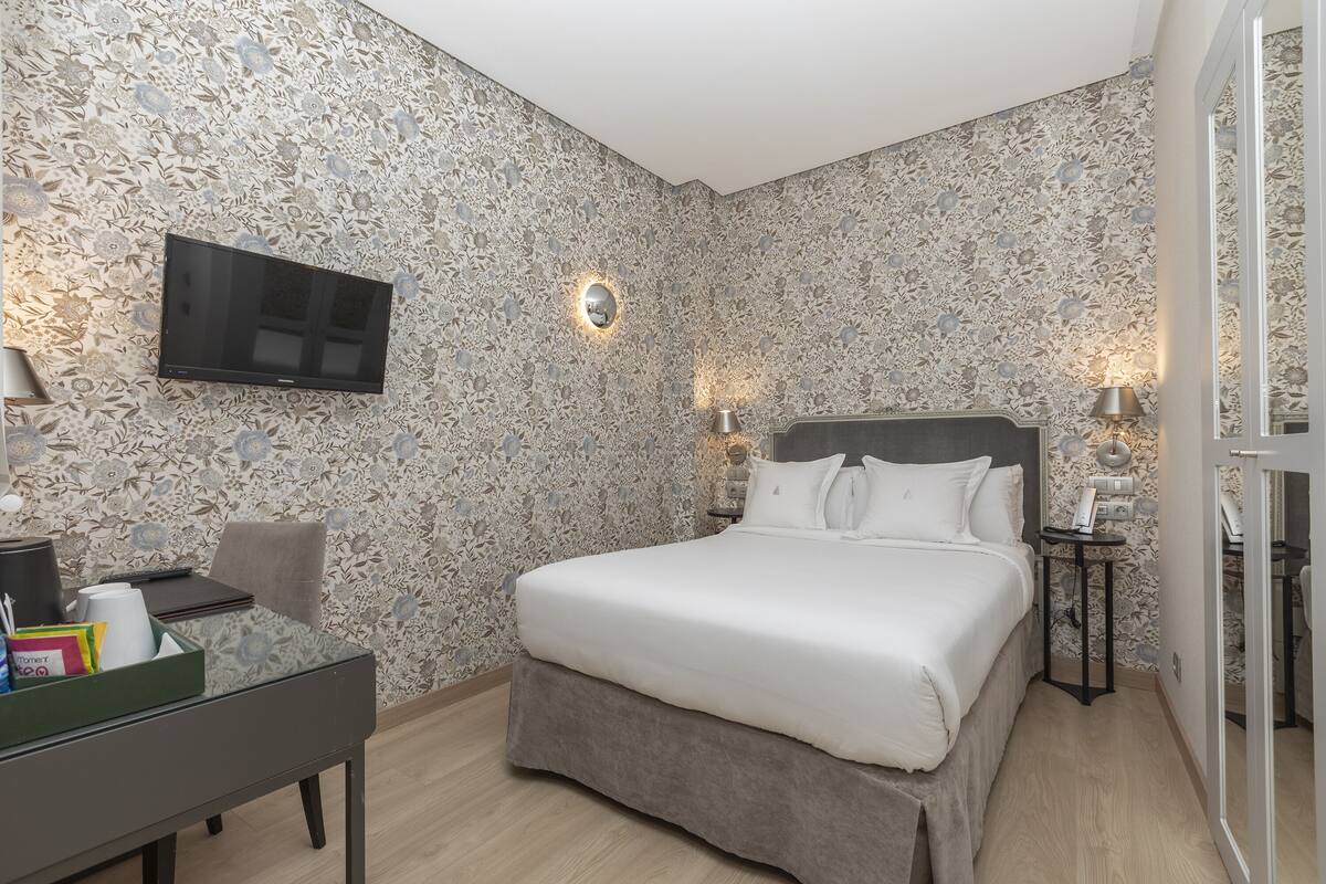 A bedroom with a large bed, a flat-screen TV mounted on the wall, and a desk with a chair.