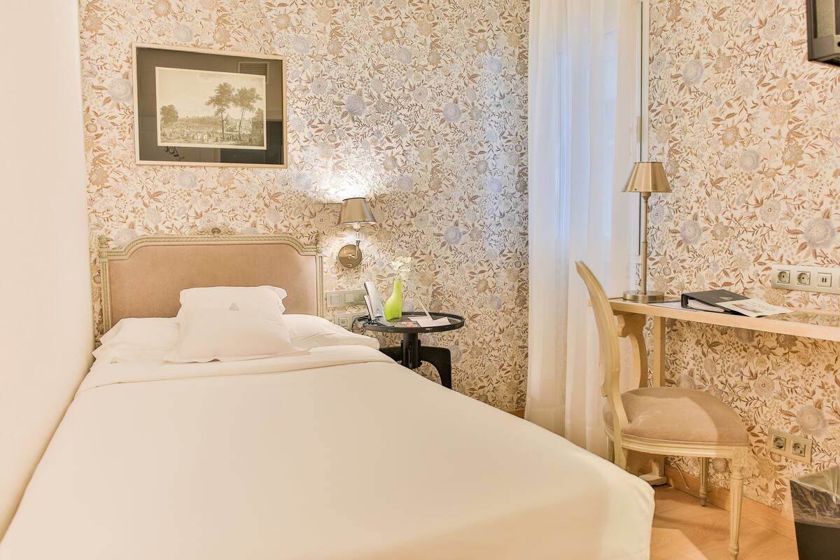 A hotel room with a bed, a desk, a chair, a lamp, and a picture on the wall.
