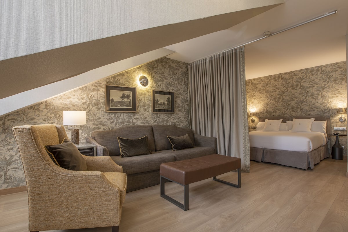 A modern hotel room with a sofa, armchair, and a bed.