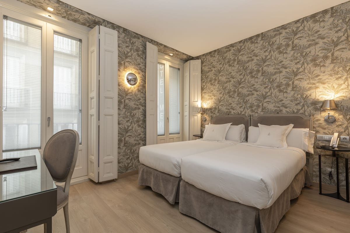 A hotel room with a double bed, a desk with a chair, and a nightstand with a lamp.