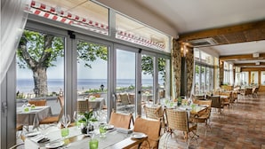 Un restaurante con mesas dispuestas para comer, amplias ventanas que dan al mar y un suelo de baldosas.