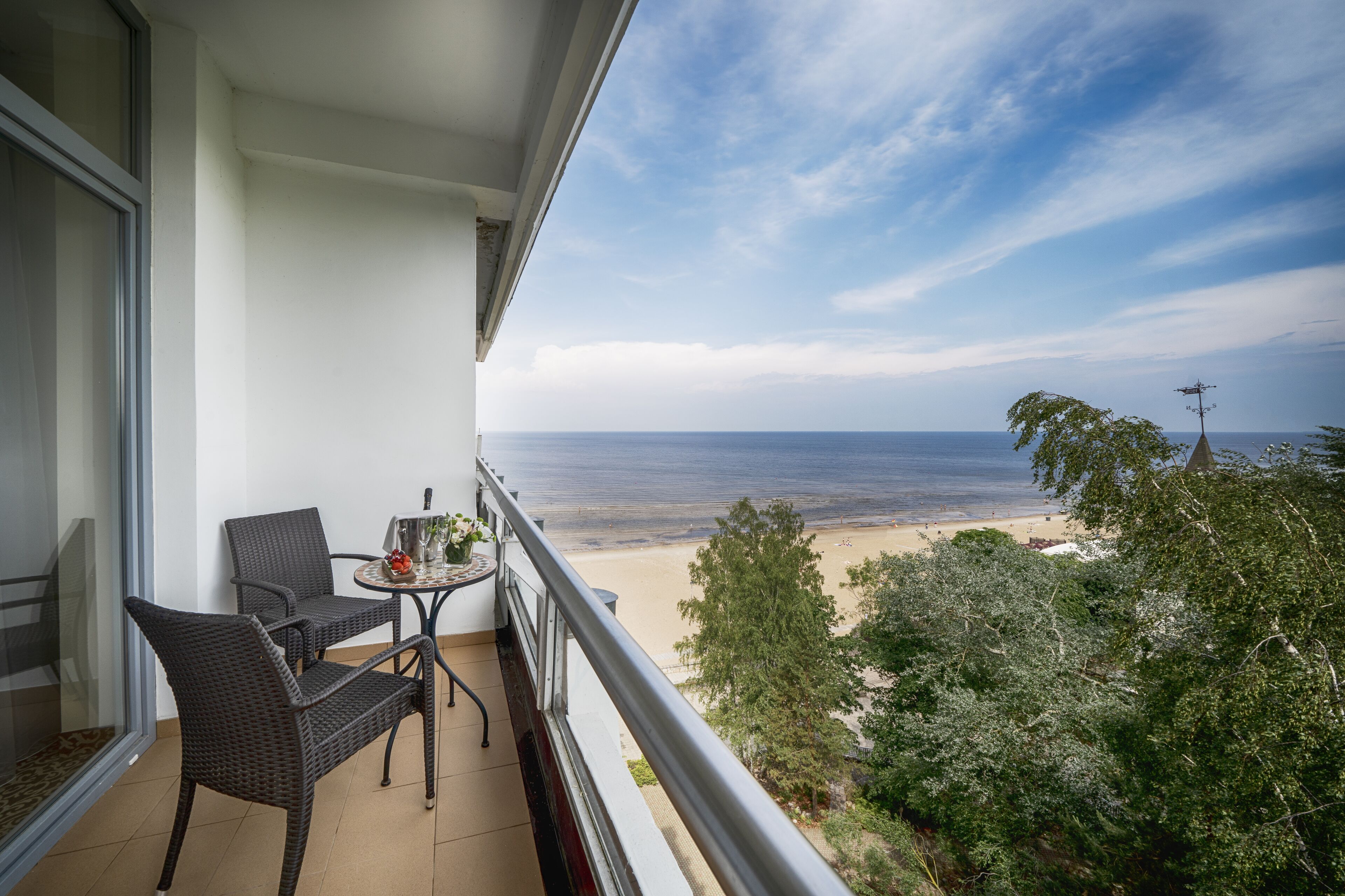 Un balcon avec des fauteuils en osier et une petite table, donnant sur une plage et l’océan.