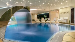 Una piscina interior moderna con diseño curvo, rodeada de sillones de descanso y un letrero que dice 'Garden'.