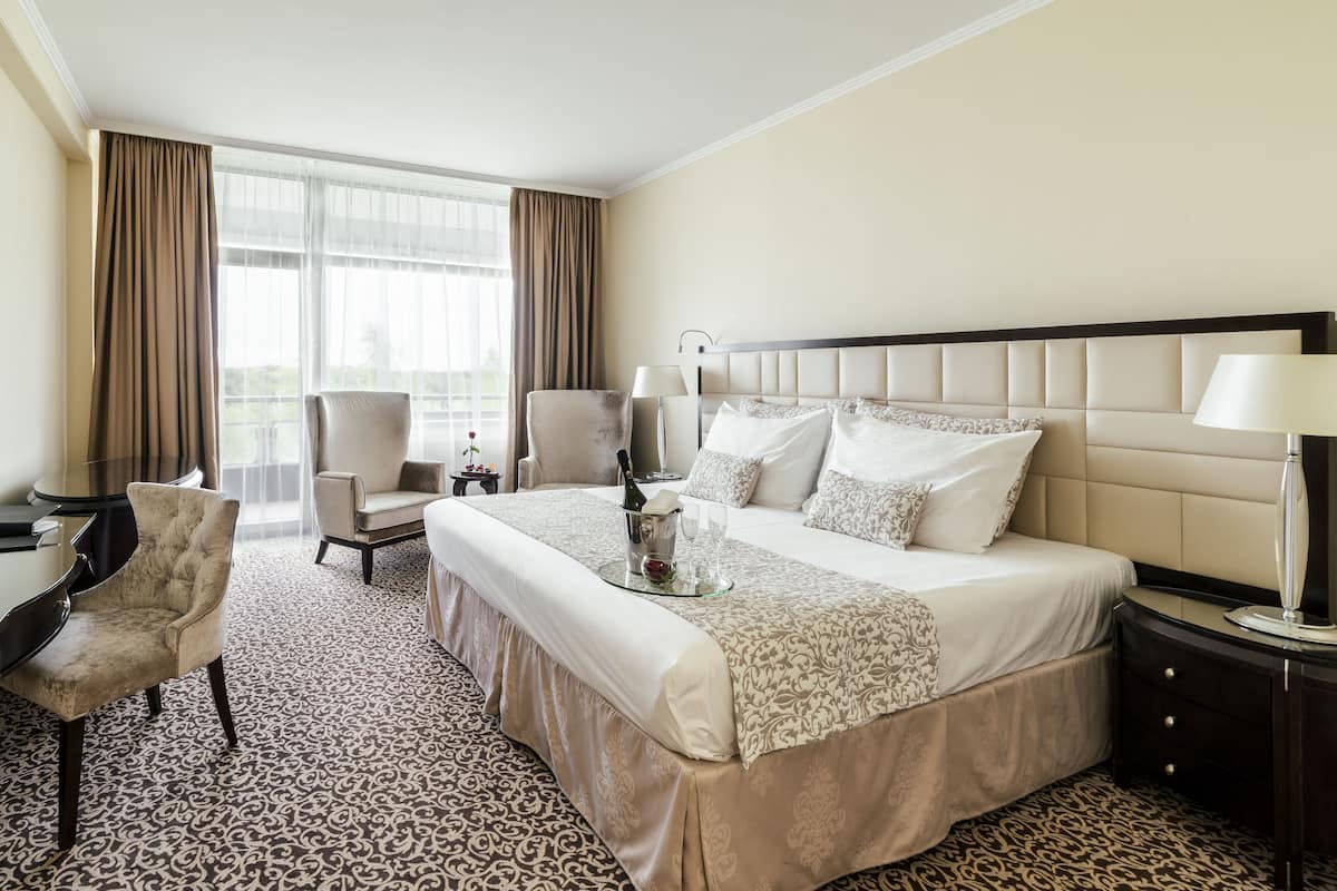 A hotel room with a large bed, two armchairs, a desk, and a nightstand.