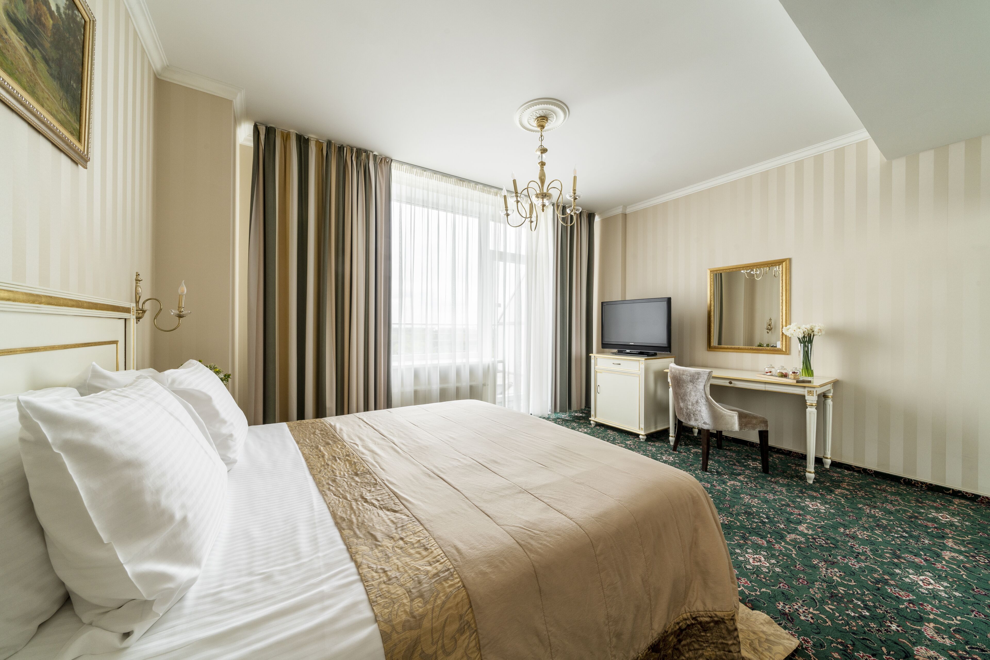 Een hotelkamer met een groot bed, een bureau met stoel, een televisie, een spiegel en een kroonluchter.