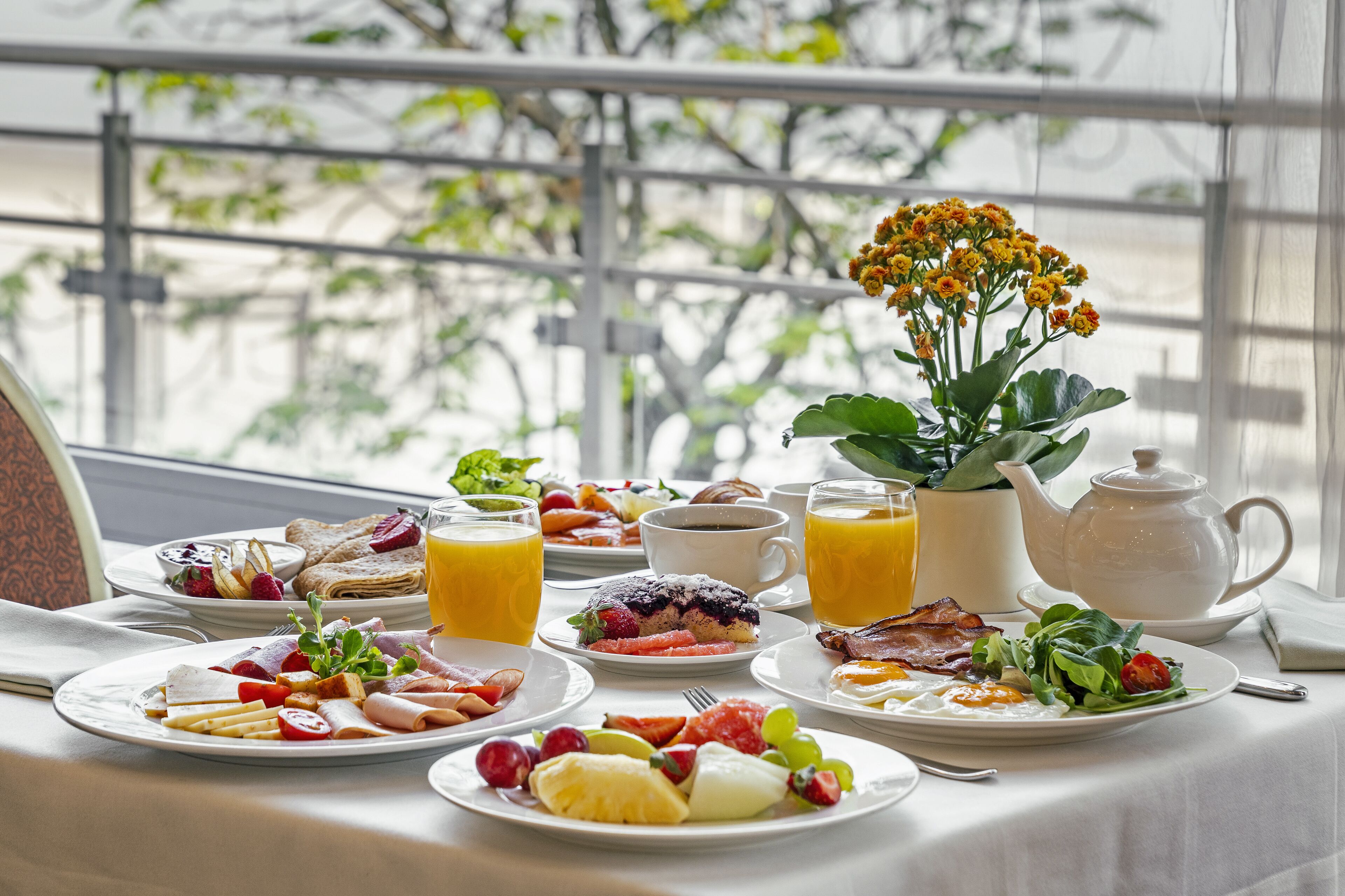 A breakfast table with various dishes, a coffee cup, a teapot, and a potted plant.