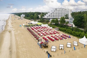 A beach with rows of red lounge chairs and umbrellas, a white building with multiple floors, and a church with a tall spire. - Baltic Beach Hotel & SPA (Jurmala)