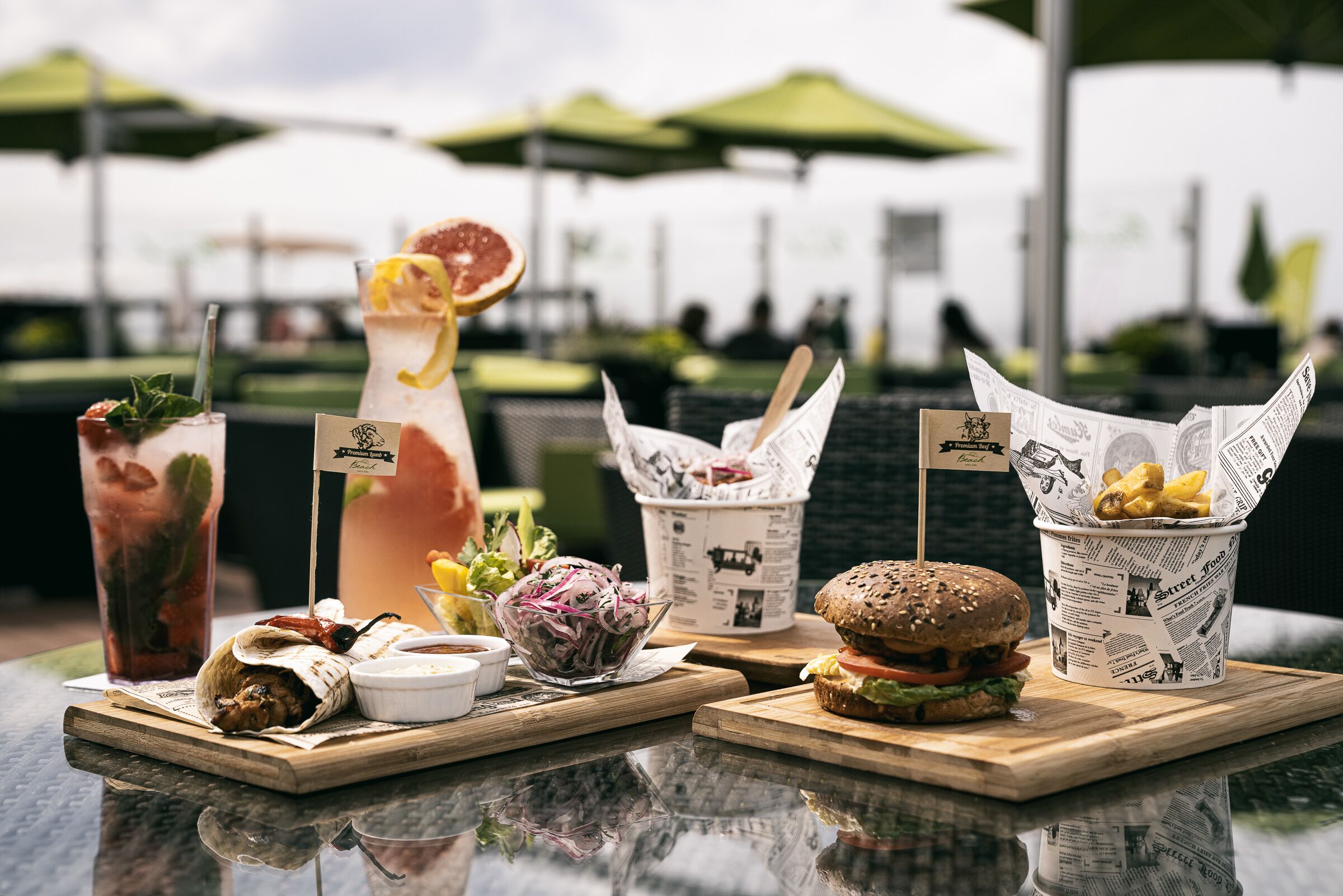 Une table sur laquelle on trouve divers aliments et boissons, notamment un hamburger, une salade et une boisson garnie d’une tranche de citron.