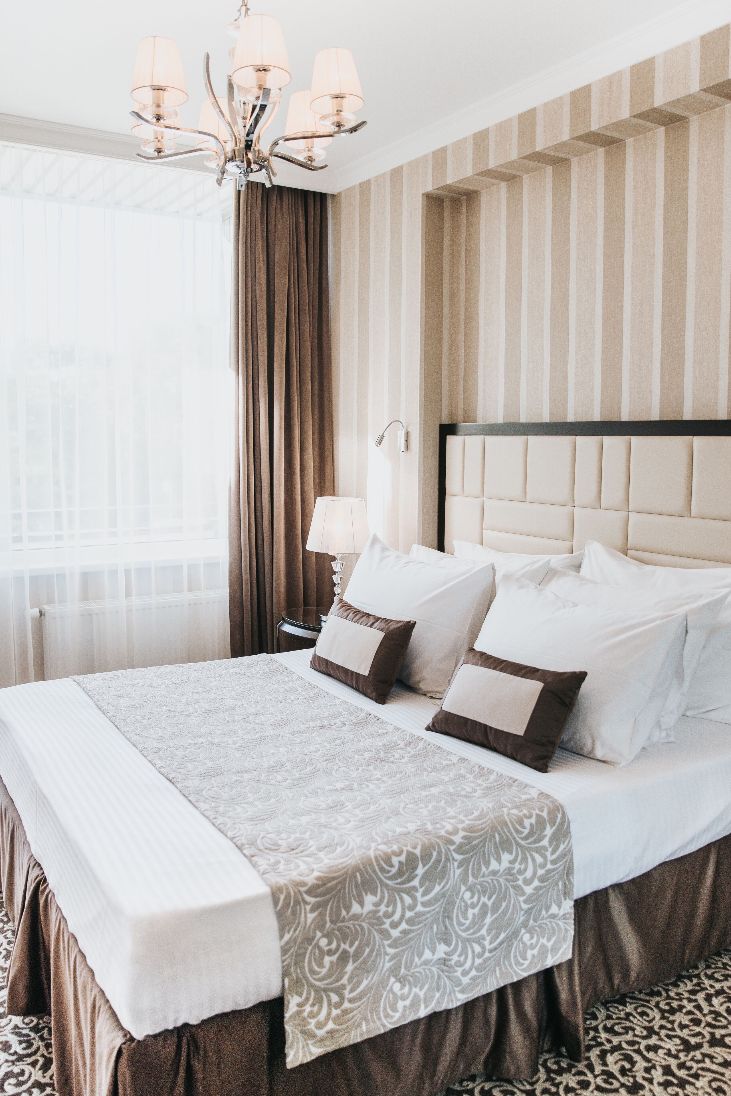 Een hotelkamer met een groot bed, een kroonluchter, een nachtkastje en uitzicht op de stad door het raam.
