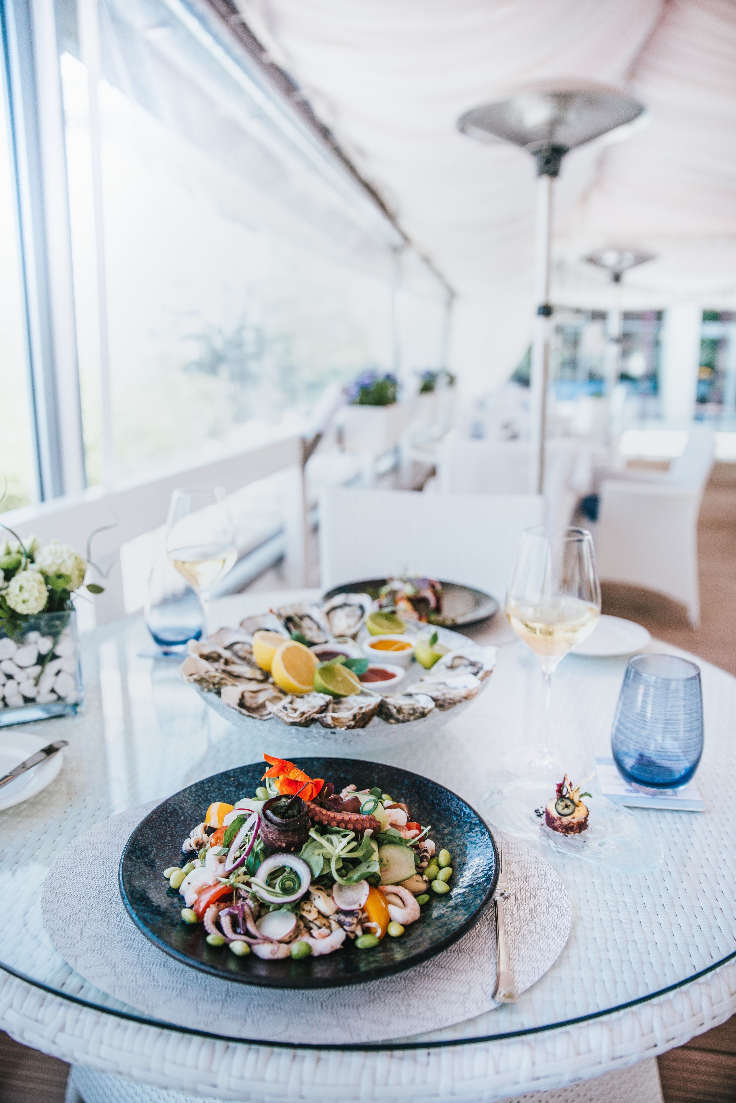 A dining table with seafood dishes, wine glasses, and a blue glass.