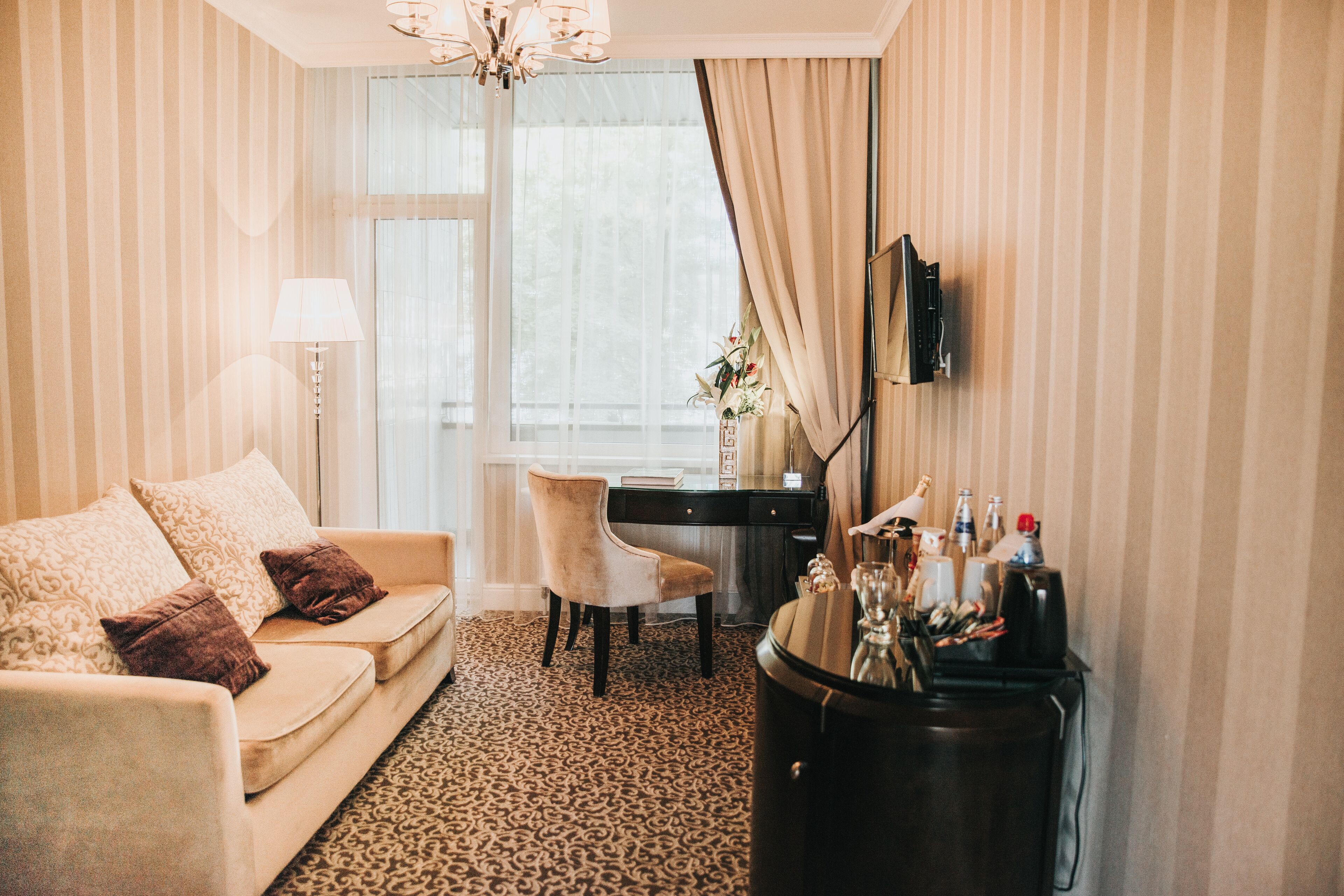 A hotel room with a sofa, a desk, a chair, a TV, and a minibar.