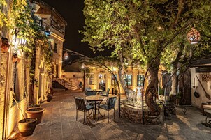 An outdoor patio with stone flooring, tables, and chairs, surrounded by buildings with ivy and potted plants.